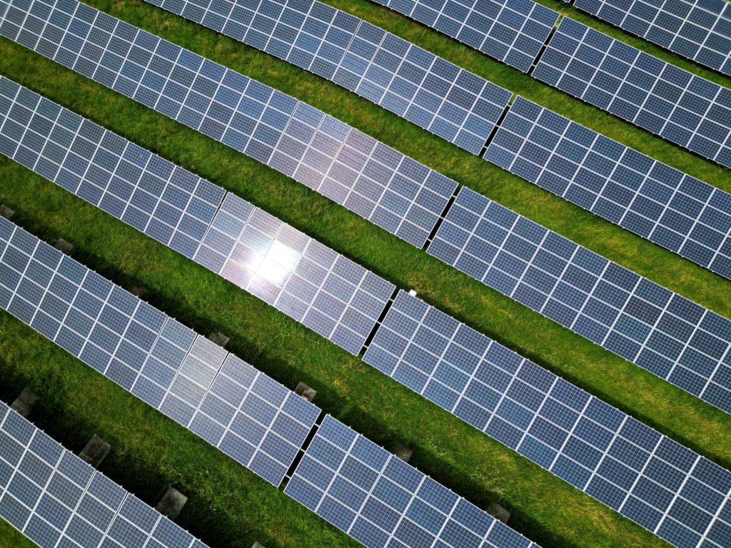 Fileiras de painéis solares em grama verde, com brilho do sol.