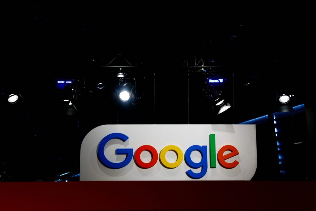 Logotipo colorido do Google em um palco escuro, iluminado por holofotes.