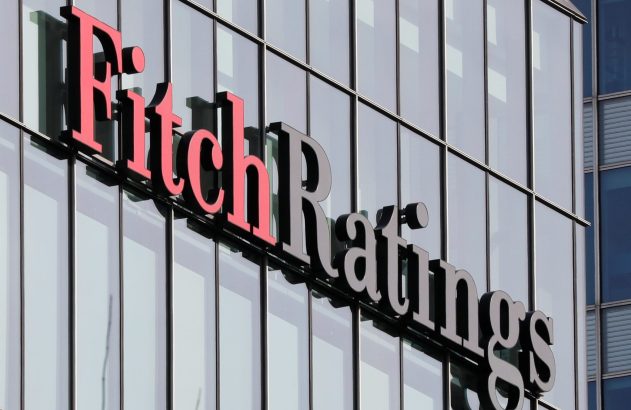 Letreiro "Fitch Ratings" vermelho e preto, 3D, em uma fachada moderna de prédio de vidro.