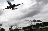 Jato comercial em aproximação sobre via com veículos. Céu nublado.