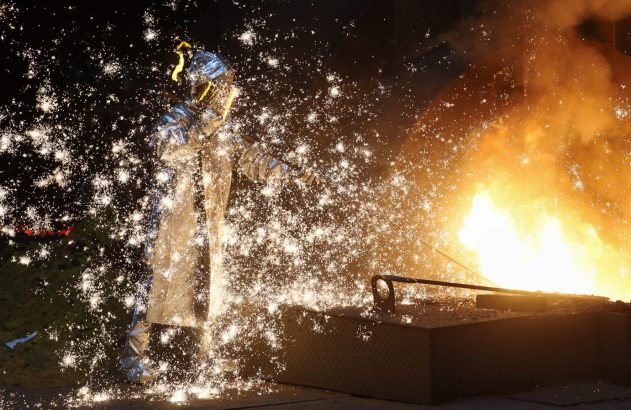Metalúrgico em traje protetor, entre faíscas intensas e brilho de metal fundido.