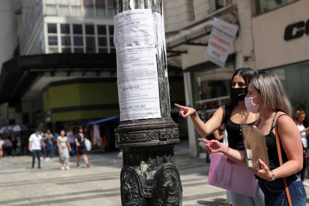 Duas mulheres apontam para avisos em um poste na rua.