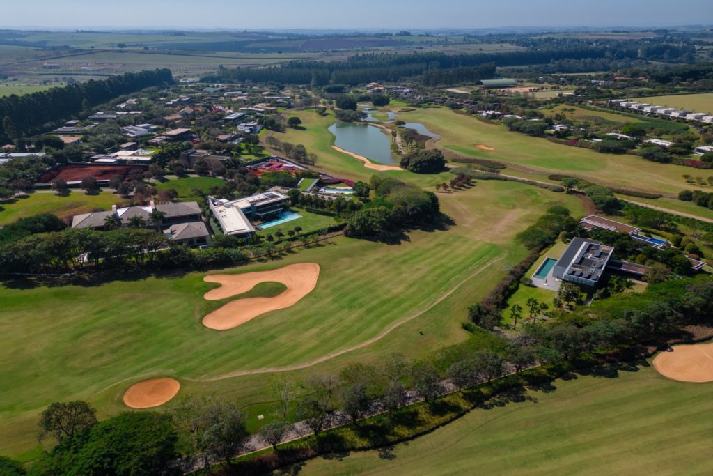 Vista aérea de campo de golfe com lago e casas.