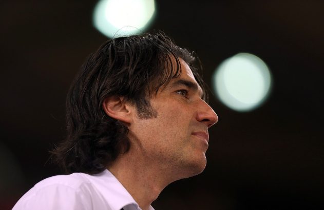 Homem de cabelo escuro, de perfil, olhando para cima. Fundo escuro desfocado com pontos de luz.