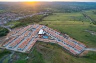 Vista aérea de conjunto habitacional novo em vale verde. Grande evento com pessoas sob tenda, pôr do sol.