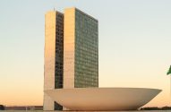 Congresso Nacional em Brasília, com suas torres, cúpula e bandeira, ao entardecer.