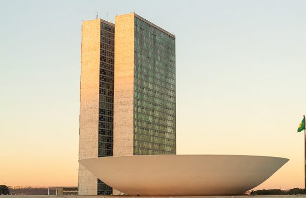 Congresso Nacional em Brasília, com suas torres, cúpula e bandeira, ao entardecer.