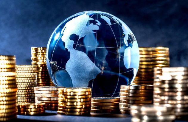 A imagem mostra o globo terrestre em azul entre várias moedas douradas. Faz parte do conteúdo sobre IVA.