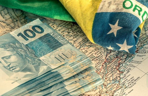 Notas de 100 reais e bandeira do Brasil sobre um mapa.