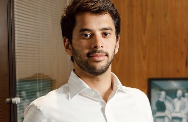 Homem jovem de camisa branca e barba, em escritório, olhando para a câmera.