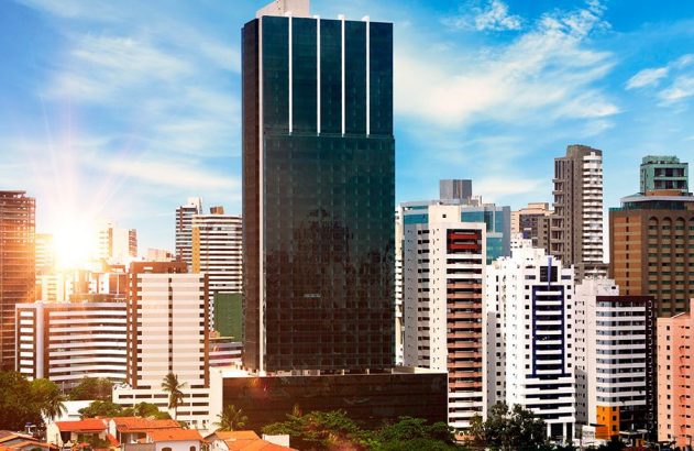 Paisagem urbana ensolarada: arranha-céus e edifícios sob céu azul com nuvens. Brilho forte do sol à esquerda.