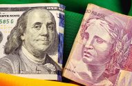 Cédulas de dólar e real lado a lado em fundo verde e amarelo.
