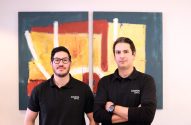 Dois homens com camisas polo Zagros Capital, em frente a quadros coloridos.
