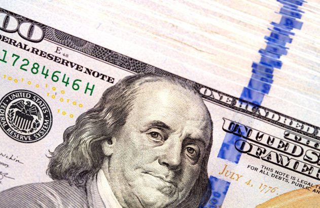 Notas de 100 dólares americanos empilhadas, com o retrato de Benjamin Franklin em destaque.