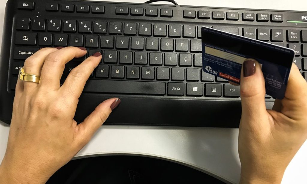 Mãos digitando no teclado e segurando um cartão de crédito.
