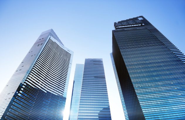 Arranha-céus modernos de vidro vistos de baixo contra um céu azul.