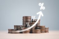 Pilhas de moedas com seta ascendente e símbolos de porcentagem, representando aumento de juros.