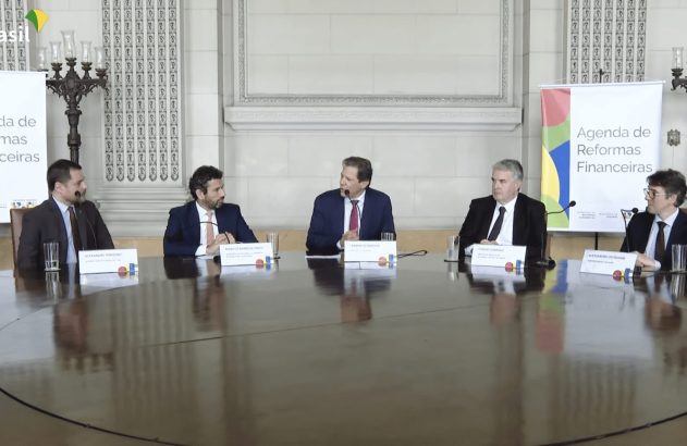 Cinco homens em ternos participam de conferência sobre reformas financeiras em uma mesa redonda.