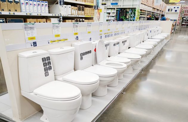 Fileira de vasos sanitários brancos em exposição num corredor de loja.