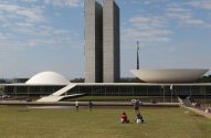 O Congresso Nacional do Brasil: edifício branco com duas torres, uma cúpula e uma semiesfera. Pessoas no gramado.