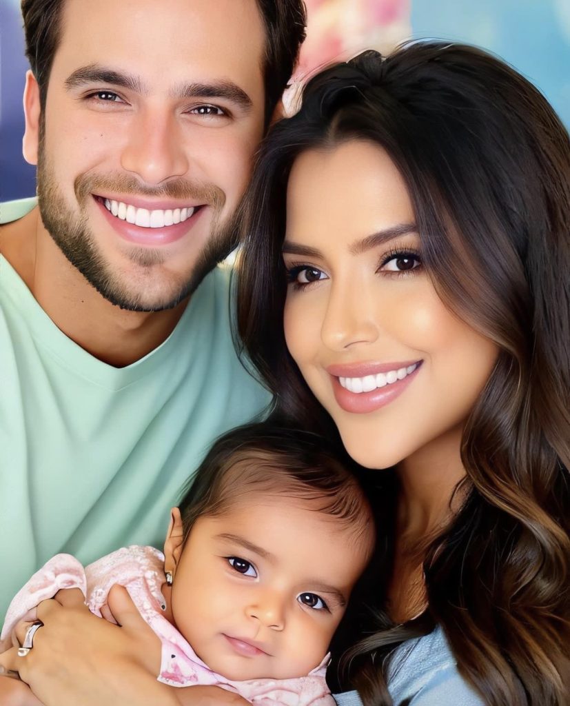 Retrato de família sorrindo: pai, mãe e bebê no colo da mãe.