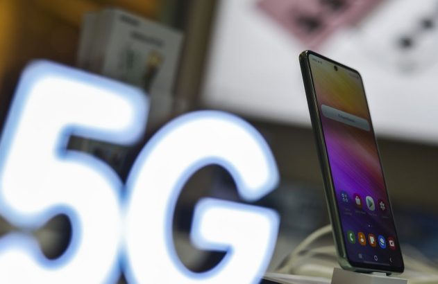 Um smartphone com tela colorida em exibição. À esquerda, um grande letreiro luminoso branco com "5G".