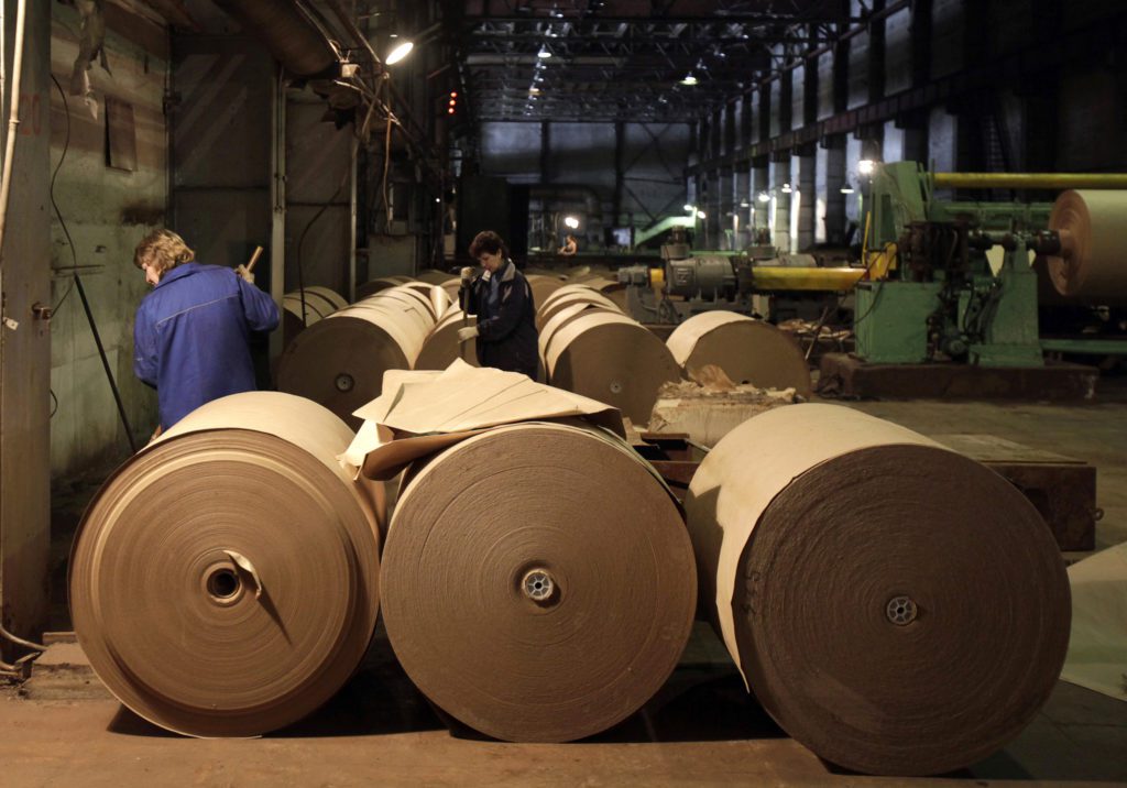 Grandes rolos de papel marrom em uma fábrica. Dois trabalhadores inspecionam a produção.