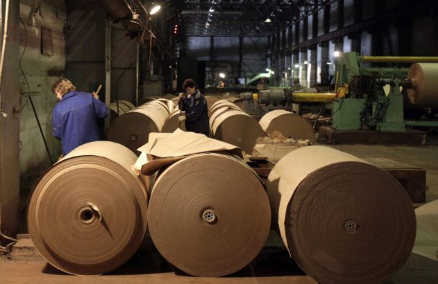 Grandes rolos de papel marrom em uma fábrica. Dois trabalhadores inspecionam a produção.