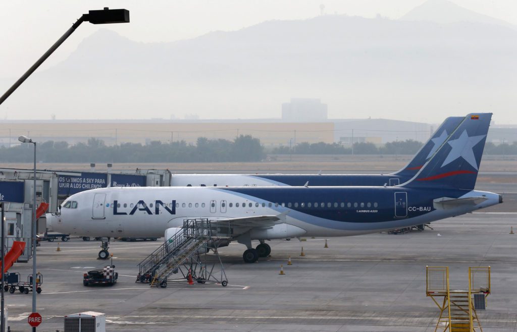 Dois aviões da LAN em um aeroporto. Um deles está no portão de embarque, com montanhas nebulosas ao fundo.