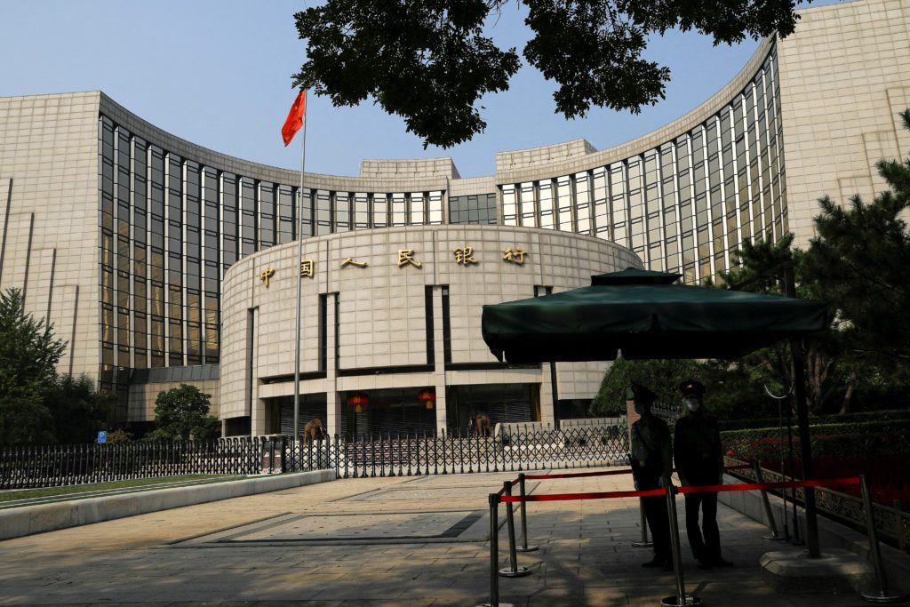 Edifício curvo do Banco Popular da China, com bandeira e dois guardas sob um guarda-sol na frente.