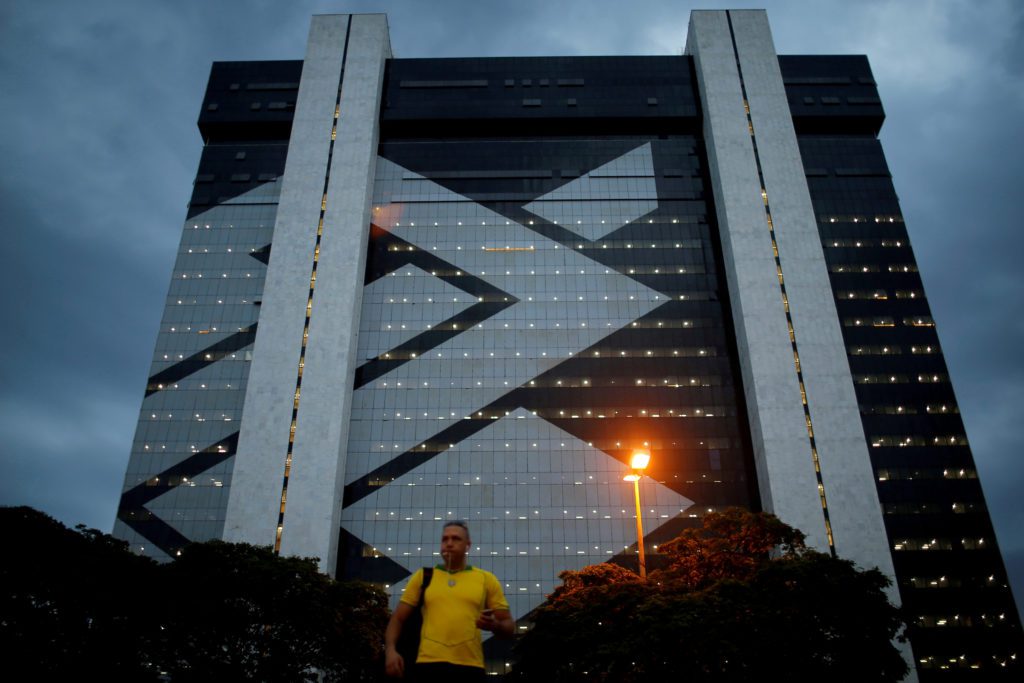 Homem caminha em frente a um grande edifício moderno com padrão geométrico iluminado à noite.