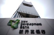 Prédio moderno. Letreiro cinza com logo verde e 'New Development Bank' em inglês e chinês na frente.