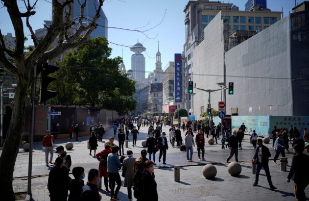 Rua movimentada com pedestres e prédios altos em um dia claro.