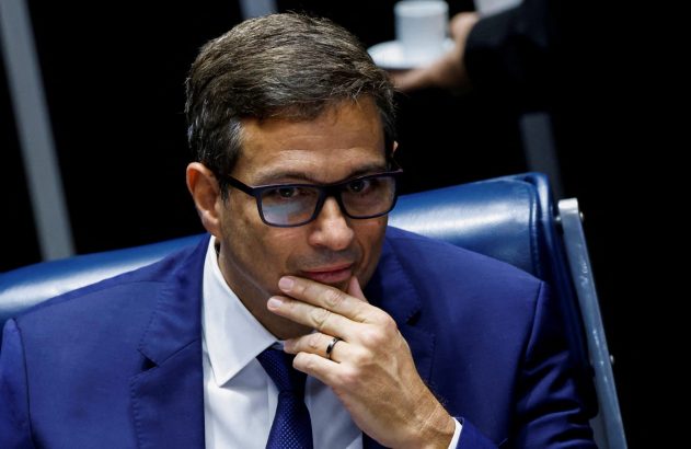 Homem de terno azul e óculos, com a mão no queixo, em atitude pensativa.