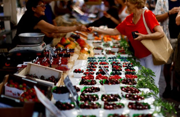 Barraca de frutas com transação entre cliente e vendedora. Diversas cerejas, amoras e framboesas expostas.