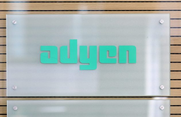 Placa de vidro fosco com o logo verde "adyen" fixada em parede de madeira clara.