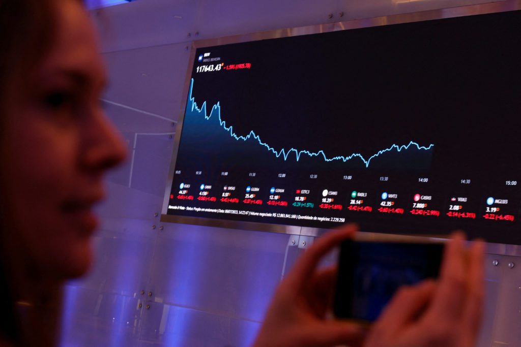 Mulher observa gráfico de queda em tela grande de dados financeiros, segurando um smartphone.