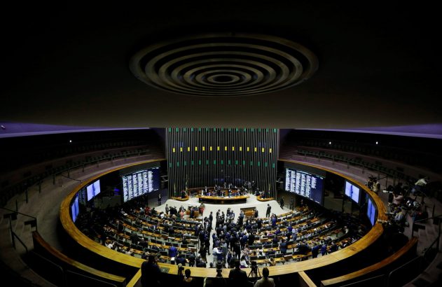 Grande plenário circular com parlamentares em sessão, monitores exibindo dados e equipe de mídia.