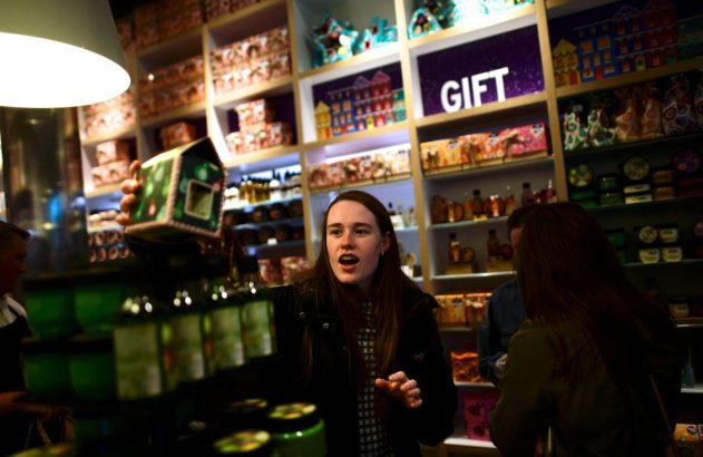 Mulher jovem em loja de presentes, reagindo a caixa em forma de casa sendo mostrada.