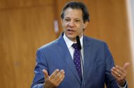 Fernando Haddad, de terno azul, fala em microfone e gesticula com as mãos.