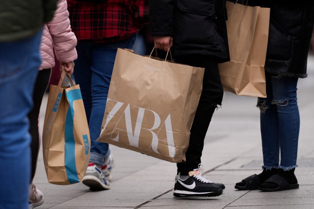 Pernas de pessoas andando com sacolas de compras, incluindo uma marrom da ZARA.