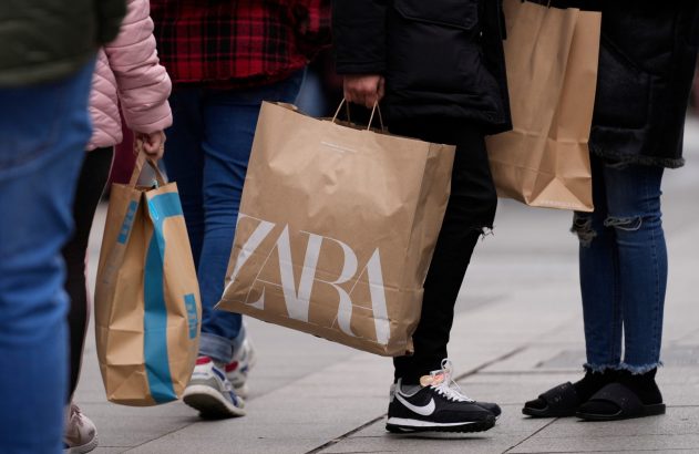 Pernas de pessoas andando com sacolas de compras, incluindo uma marrom da ZARA.