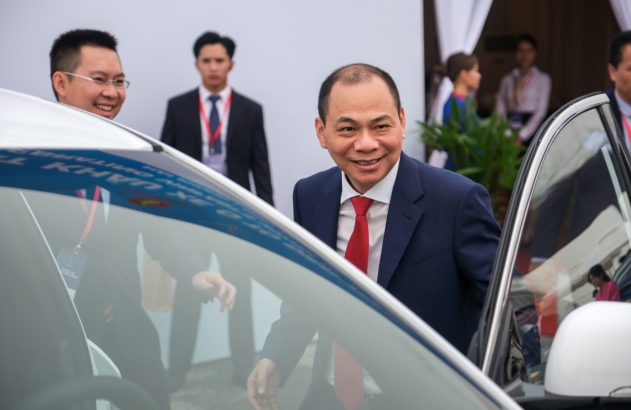 Homem sorridente de terno e gravata vermelha entrando em carro branco.