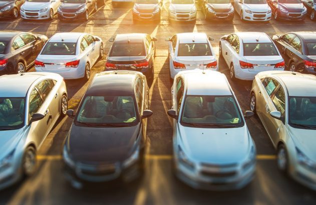 Fileiras de carros estacionados em um pátio, sob a luz dourada do sol.
