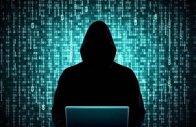 Hacker encapuzado em silhueta, usando laptop com fundo de código binário.