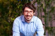 Homem de óculos, barba e suéter azul, com braços cruzados.