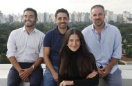Quatro pessoas (uma mulher, três homens) sorrindo, sentadas em um terraço com vista para a cidade.