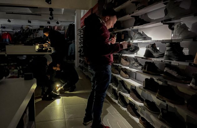 Loja de sapatos no escuro, clientes usam luzes de celular e lanternas para escolher calçados.