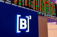 Painel digital de bolsa de valores exibindo cotações e o logo da B3 iluminado.