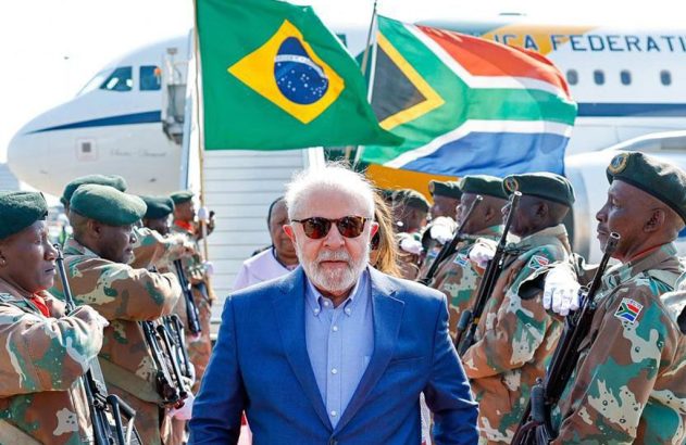Lula em recepção militar na África do Sul, com soldados e bandeiras do Brasil e da África do Sul.